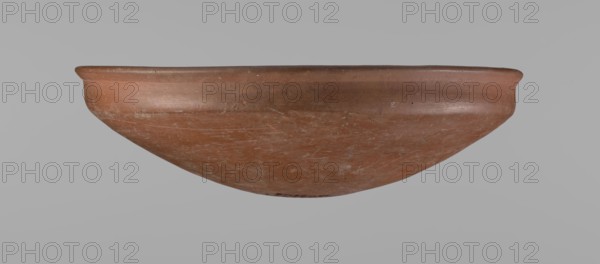 Medum-type bowl, Egyptian ceramics, Medum-type bowl with characteristic carination under the rim. Rounded bottom. Straight rim, slightly flaring. Narrow, very sloping shoulders—almost vertical. The diameter of the rim is larger than the diameter of the shoulders of the vessel. Clay probably NB. Surface leveled and covered with a layer of engobe, then polished. Vessel color red. Vessel complete, very well preserved. Comparative material: Junker, Giza I, pl. I,2,16, c. 2686–c. 2181 BC; Old Kingdom late Old Kingdom, Edfu; vessel height 7.5 cm, diameter 25.8 cm rim, diameter 25.2 cm shoulders., A shallow, rounded bowl with a wide rim is centered against a plain light gray background; the bowl has a smooth terracotta surface in shades of reddish-brown and muted orange with lighter scuff marks and darker spots, a gently flared lip, and a worn, slightly uneven finish visible across its curved exterior.