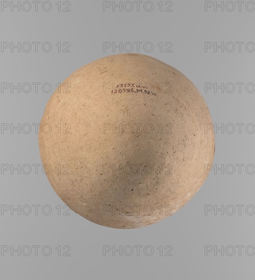 Vessel, Ovoid, slightly downward-stretched clay vessel, widest at about 2/3 of the height. Broad shoulders, very short wide neck; roller-shaped rim oval in cross-section and slightly flaring; rounded bottom. Handcrafted from two parts joined at about 2/3 of the height, upper part turned. Surface leveled; traces of a white substance on outer surface and rim. Clay with significant organic admixture Viennese System. Beige color. Complete, well-preserved. Late Old Kingdom ca. 2686–2181 BC. From Edfu. Height 24.9 cm; rim diameter 10.2 cm; body diameter 20.7 cm., A large round object with a rough, textured surface in beige and tan tones sits against a smooth light gray background; the object shows small dark specks and fine irregular marks across its surface, subtle variations in shading with slightly darker beige areas and faint off-white patches near the lower edge, and a small area near the top with darker brown and muted purple marks.