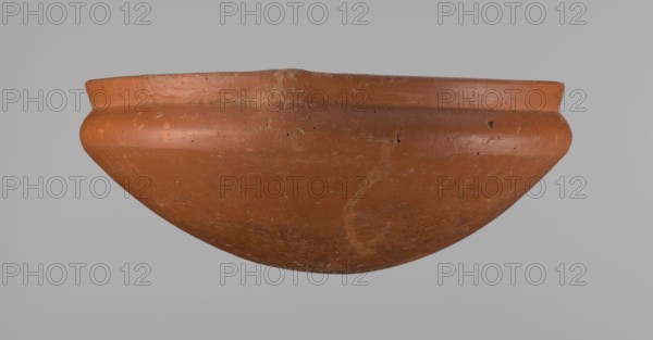 Medum-type bowl, Medum-type bowl with characteristic carination under the rim. Rounded bottom. Straight, slightly flaring rim. Narrow, sloping shoulders. The diameter of the rim is smaller than the diameter of the vessel's shoulders. Surface leveled and covered with a layer of engobe, then polished. Vessel color: red. Vessel cracked and glued together; minor clay losses on the rim filled with plaster. Ca. 2686–ca. 2181 BC; Old Kingdom 6th Dynasty?. From Edfu. Vessel; height 8.9 cm, diameter 21.7 cm rim, diameter 22.3 cm shoulders., A rounded clay bowl shown from the side with a flared rim and a curved body, displaying an overall terracotta color with areas of darker and lighter brownish-orange, a few small chips and surface imperfections, subtle streaks and spots of lighter beige residue, and a neutral gray background.