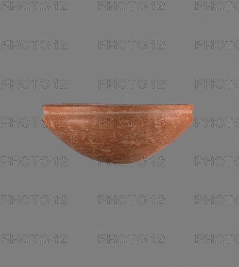 Medum type bowl, Egyptian ceramics, Medum type bowl with characteristic carination under the rim. Rounded bottom. Straight rim, slightly flaring. Narrow, sloping shoulders. The diameter of the rim is smaller than the diameter of the vessel's shoulders. Clay probably NB1. The surface is leveled and covered with a layer of engobe, then polished. Vessel colour red. Complete vessel, very well preserved. c. 2686–c. 2181 BC; Old Kingdom, Edfu. Vessel; height 4.2 cm, diameter rim 21.1 cm, diameter shoulders 21.1 cm., A single terracotta bowl with a rounded shape and a slightly thickened rim sits against a plain gray background; the bowl shows a weathered surface with patches of lighter and darker reddish-brown, small worn spots, and faint horizontal lines around its exterior, and the visible colors include reddish-brown, lighter beige areas from wear, and gray in the background.