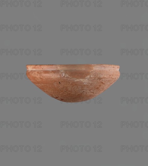 Medum type bowl. Medum type bowl with characteristic carination under the rim. Rounded bottom. Straight rim, slightly flaring. Narrow, sloping shoulders. The diameter of the rim is smaller than the diameter of the vessel's shoulders. Clay probably NB1. The surface of the vessel is leveled and covered with a layer of engobe, and then polished. Vessel colour - red. Complete vessel, very well preserved. c. 2686–c. 2181 BC; Old Kingdom, Edfu. Vessel; height 4.2 cm; diameter rim 21.1 cm; diameter shoulders 21.1 cm., A rounded shallow bowl with a worn, textured surface in shades of reddish-brown and terracotta, showing patches of lighter beige and white wear, floating against a flat gray background.