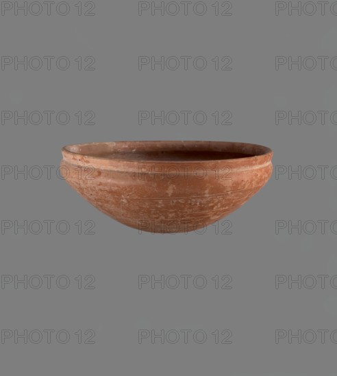 Medum type bowl. Medum type bowl with characteristic carination under the rim. Rounded bottom. Straight rim, slightly flaring. Narrow, sloping shoulders. The diameter of the rim is smaller than the diameter of the vessel's shoulders. Clay probably NB1. Surface leveled and covered with a layer of engobe, then polished. Vessel color: red. Complete vessel, very well preserved. c. 2686–c. 2181 BC; Old Kingdom, Edfu. Vessel. Height 4.2 cm; diameter rim 21.1 cm; diameter shoulders 21.1 cm., A shallow rounded bowl with a worn, textured surface in terracotta tones of reddish-brown and orange, showing lighter patches and scuffed areas; the bowl has a slightly raised rim and subtle horizontal tool marks, photographed against a uniform mid-gray background.
