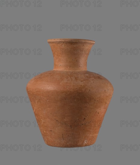 Jug, Egyptian pottery jug, cylindrical with flaring neck, clay, c. 2686–c. 2181 BC Old Kingdom, from Edfu; vessel height 18.6 cm, rim diameter 8.5 cm, body diameter 15.8 cm, bottom diameter 9.1 cm., A single clay vessel with a rounded body that tapers toward the base and rises to a flared neck, shown against a plain background. The vessel is predominantly terracotta brown with variations in tone and small dark speckles and fine surface cracks. The background is a uniform gray. The surface of the clay shows rough, slightly weathered texture and a few lighter and darker spots.