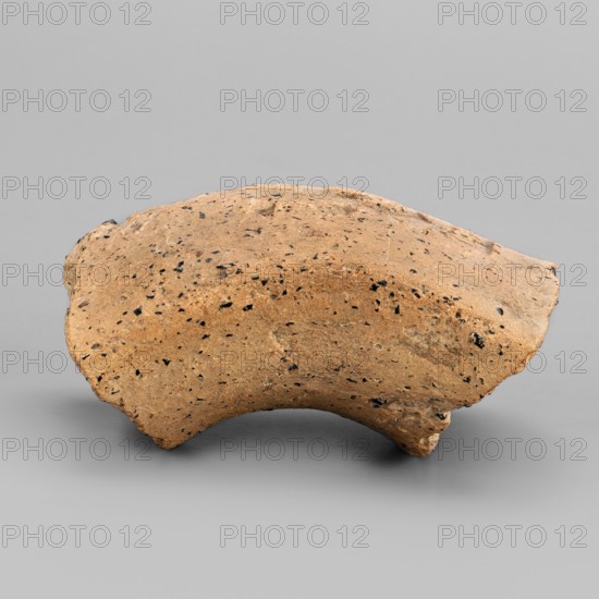 Fragment of an amphora vice behind a stamp, Sinope Asia Minor uncertain determined by AT and did not provide a bibliography, gift, 4th–beginning of 3rd century BC, Pantikapaion, vessel, height 4.1 cm, width 6.3 cm, A roughly rounded, irregularly shaped object with a sandy brown surface speckled with several small dark spots rests on a smooth light gray background; the object has a curved underside and uneven edges with a few rougher, slightly darker brown areas and tiny lighter flecks, casting a soft shadow on the gray surface beneath it.