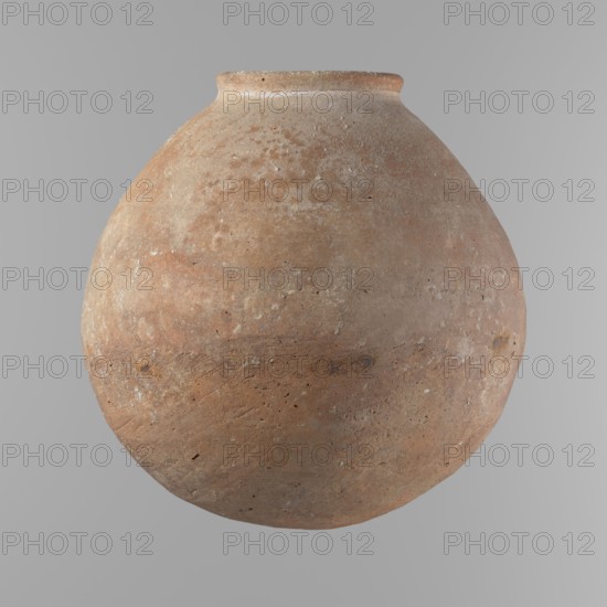 Vessel, Egyptian ceramic vessel with an almost spherical belly, widest about 1/3 of the vessel's height; sloping shoulders; poorly defined, very short and wide neck; rounded, slightly flaring rim; rounded bottom. Made of Nile clay NB. Surface smooth; outer surface finished to about half its height with a knife or similar tool; a rather indistinct cord impression around the widest diameter of the belly. Light red color. Chipped rim and traces of salting over the surface. Comparative typology: Old Kingdom, ca. 2686–2181 BC; provenance Edfu. Dimensions: height 24.9 cm; rim diameter 10.3 cm; body diameter 24.2 cm., A large round clay vessel with a narrow rim sits against a plain gray background; the vessel shows an uneven, weathered surface in shades of brown, tan, beige, and muted orange with patches of lighter off-white speckling, rough texture, small pits, and subtle horizontal striations.