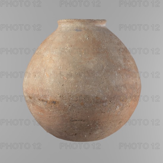 Vessel, Vessel with an almost spherical belly, widest about 1/3 of the vessel's height. Sloping shoulders. Neck poorly defined — very short and wide. Rounded, slightly flaring rim. Rounded bottom. Made of Nile clay NB. Surface smooth; outer surface finished to about half its height with a knife or similar tool. A rather indistinct cord impression around the widest diameter of the belly. Light red color. Chipped rim and traces of salting in places over the entire surface. Comparative typology: type II/III, ca. 2686–2181 BC; Old Kingdom, Edfu. Vessel height 24.9 cm; rim diameter 10.3 cm; body diameter 24.2 cm., A large rounded clay vessel with a narrow rim, showing a rough, weathered surface texture and small pits and speckles; the vessel displays shades of brown, tan, beige, and hints of warm reddish-orange, with areas of lighter off-white encrustation and faint darker brown marks.