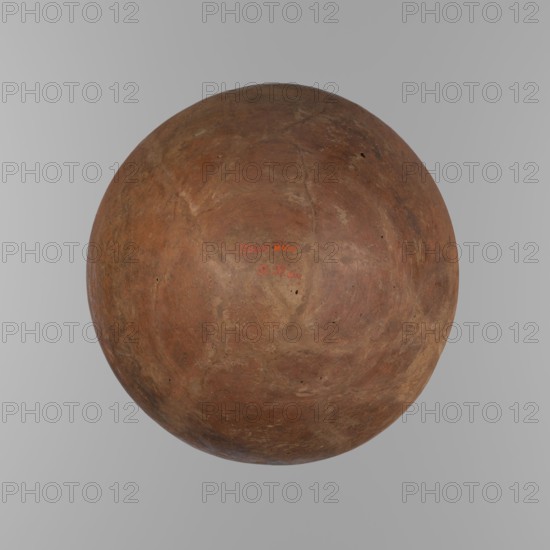 Bowl. Large conical clay vessel with rounded bottom and straight, slightly tapering spout. Widest about 4/5 of the height, walls narrowing toward center. Just below the rim two parallel horizontal shallow lines. Made of Nile clay NB2 Vienna System. Surface leveled and covered with red engobe; overall dark red color. Reconstructed from original fragments with losses including significant rim fragments filled with plaster. Possibly end of ST.P beginning of 1st OP. Attributed references: F. Petrie, Medum, pl. XXXI, fig. 3; A. Fakhry, The monuments of Sneferu at Dahshur, p. 116, figs. 7-5, c. 2686–c. 2181 BC. Old Kingdom, Edfu. Vessel height 21.4 cm; rim dia. 28.5 cm; shoulder dia. 30.5 cm., A large round object with a rough, mottled surface fills the image; the object shows a range of earthy browns, reddish-browns, and tan patches with a few darker brown spots and subtle lighter beige areas, and it sits against a smooth light gray background.