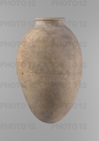 Vessel, unknown creator; ceramics, Egyptian clay vessel with ovoid belly, widest about halfway up. Wide, short, almost cylindrical neck; rounded, slightly tapering rim; rounded bottom. Made of Nile clay in two parts joined about one-third of the vessel's height. Surface even; beige color; complete. Comparative material: type V–XI,7 and XV–XVI Reisner, ca. 2686–2181 BC; Old Kingdom, Edfu; vessel height 35.5 cm, rim diameter 10.2 cm, body diameter 22.2 cm., A single large rounded jar with a narrow rim and bulbous body fills the image, showing a textured surface in shades of beige, tan, light brown, and muted gray, with darker speckles and subtle variations in tone across its weathered exterior.