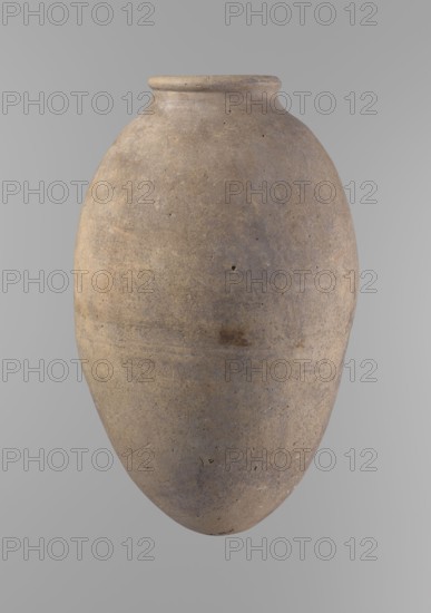 Vessel, Egyptian ceramics, clay vessel. Vessel with an ovoid belly, widest about halfway up; wide, short, almost cylindrical neck; rounded, slightly tapering rim; rounded bottom. Made of Nile clay in two parts joined about one-third of the vessel's height. Surface even, beige color, complete. Comparative material: Reisner, Mycerinus, type V–XI,7 and XV–XVI, fig.65,7 fig.67,1–2, ca. 2686–2181 BC; Old Kingdom, Edfu; vessel height 35.5 cm, diameter 10.2 cm rim, diameter 22.2 cm body., A large rounded ceramic vessel with a narrow neck and slightly flared rim, shown against a plain neutral background; the surface of the vessel appears textured and weathered with a mottled mix of beige, brown, gray, and subtle olive tones, showing small pits, scratches, and patches of darker discoloration, and an overall matte finish.