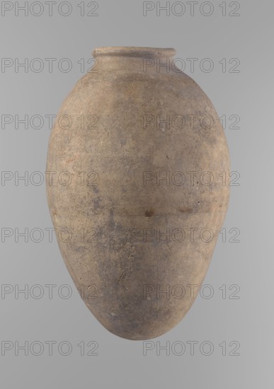 Vessel with an ovoid belly, widest about halfway up. Wide, short, almost cylindrical neck with a rounded, slightly tapering rim and rounded bottom. Made of Nile clay in two parts, joined about one-third of the vessel's height. Even surface, beige color, complete. Ceramic Egyptian vessel, clay vessel; height 35.5 cm, rim diameter 10.2 cm, body diameter 22.2 cm. Old Kingdom, Edfu, ca. 2686–2181 BC. Comparative typology: Reisner, Mycerinus, type V–XI,7 and XV–XVI., A large rounded ceramic jar with a narrow, slightly flared neck and a rounded base, shown against a plain light gray background; the jar surface appears textured and weathered with a mix of earthy browns, muted tans, and subtle grayish tones, with a few darker spots and faint variations in color across its surface.