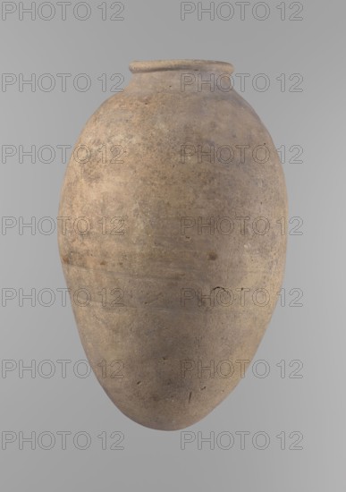 Vessel, Ceramics, Egyptian clay vessel with an ovoid belly, widest about halfway up. Wide, short, almost cylindrical neck; rounded, slightly tapering rim; rounded bottom. Made of Nile clay in two parts joined about one-third of the vessel's height. Surface even, beige color, complete. Comparative typology: Reisner, Mycerinus, type V–XI,7 and XV–XVI ca. 2686–2181 BC; Old Kingdom, Edfu. Dimensions: height 35.5 cm; rim diameter 10.2 cm; body diameter 22.2 cm., A large rounded ceramic vessel with a narrow neck and slightly flared rim fills the image, showing a textured surface with a weathered, uneven finish. The vessel displays a mix of earthy colors including beige, tan, light brown, and subtle grayish tones, with darker brown speckles and faint patches of muted ochre. The surface has small pits, scratches, and irregular marks, and there are a few horizontal ridges and shallow depressions visible around the midsection. The background is a smooth, even light gray.