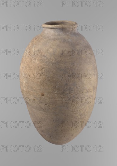 Vessel with an ovoid belly, widest about halfway up. Wide, short, almost cylindrical neck. Rounded, slightly tapering rim. Rounded bottom. Made of Nile clay in two parts joined about one-third of the vessel's height. Surface even, beige color. Complete. Ceramic Egyptian vessel, clay vessel; Old Kingdom, ca. 2686–2181 BC, Edfu. Height 35.5 cm; diameter 10.2 cm rim, 22.2 cm body. Comparative type: Reisner, Mycerinus, type V–XI,7 and XV–XVI., A large rounded clay vessel with a narrow neck and flared rim, shown against a plain light gray background; the vessel surface is rough and weathered with a mottled palette of brown, tan, beige, and hints of gray, displaying irregular patches, small pits, and subtle textured variations across its curved body.