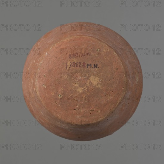 Jug, ceramics, Egyptian clay vessel jug — small jug with one handle; widest about 2/3 of the vessel's height. Wide, rather sloping shoulders; short neck widening toward the spout; straight, slightly flaring spout. Lower handle attached slightly above the vessel's widest diameter; upper attachment reaches the spout, protruding 1 cm above the spout line. Handle circular in cross-section on the lower part, slightly flattened in the upper part. Slightly convex bottom. Made of Nile clay. Surface even and covered with a thick layer of red slip on the outside and on the rim and neck inside. Color red-brown. Complete and fairly well preserved; slip worn away in places. Dating and origin: ca. 2686–2181 BC, Old Kingdom; Edfu. Measurements: height 12.7 cm; rim diameter 8.4 cm; body diameter 13.5 cm; bottom diameter 9.5 cm. Analogies: A. Fakhry, The Monuments of Sneferu at Dahshur, figs. 4–4., A round, shallow vessel viewed from above with a textured, worn surface showing earthy tones of reddish-b...