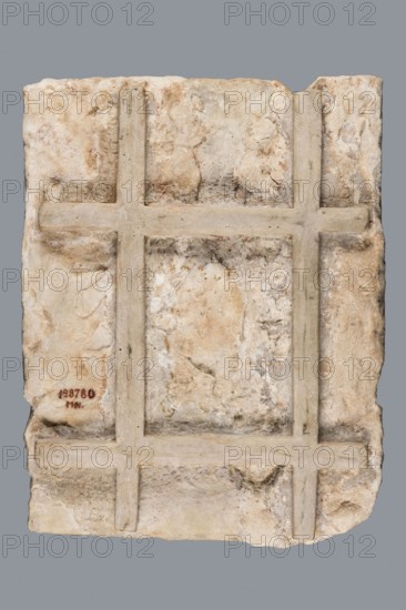Greek dedicatory inscription, unknown author. To the Savior Gods Dioskuros Artemidoros son of Anubatos and his wife-sister Heraklia called also Tsinyris and son Hermanubis called also Dioscorides gave the grace of piety for happiness hedera. 1st half of the 1st century BC, Egypt. Greek inscription. Height 40 cm, width 30 cm, depth 2 cm., A roughly rectangular slab with a weathered, uneven surface showing a grid-like relief of raised bands forming rectangular compartments; colors visible include various shades of beige, cream, off-white, light tan, pale brown, and touches of gray and faint green, all set against a solid medium-gray background.