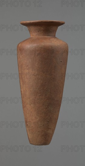 Vessel, Egyptian pottery, Type HS vessel of conical, slender shape, widest at about 3/4 of the height. Shoulders quite wide, almost horizontal, slightly sloping. Neck wide, short, funnel-shaped in its lower part, widening towards the rim from about half its height. Rim wide, flat in the upper part, slightly rounded at the bottom, slightly asymmetrical. Bottom flat, slightly asymmetrical. Neck made separately and glued to the shoulders. Surface even. Lower part finished to approximately 3/4 of its height using a knife or similar tool. Outer surface and inner surface of the rim and neck covered with a layer of dark red engobe and polished. Color dark red. Reconstructed from many original fragments; gaps filled with plaster. c. 2686–c. 2181 BC; Old Kingdom; Edfu. Vessel; height 24.8 cm; diameter 8.9 cm rim; diameter 10.3 cm shoulders; diameter 4.1 cm bottom., A tall, narrow vessel with a flared rim and a gently rounded shoulder tapering to a pointed base, made of a rough, porous material ...