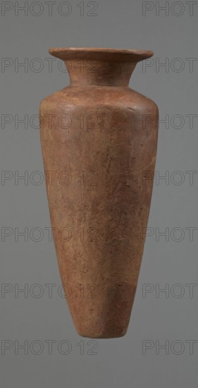 Vessel, Egyptian pottery, Type HS vessel of conical, slender shape, widest at about 3/4 of the height. Shoulders wide, almost horizontal, slightly sloping. Neck wide, short, funnel-shaped in its lower part, widening towards the rim from about half its height. Rim wide, flat in the upper part, slightly rounded at the bottom, slightly asymmetrical. Bottom flat, slightly asymmetrical. Neck made separately and attached to the shoulders. Surface even. Lower part finished to approximately 3/4 of its height using a knife or similar tool. Outer surface and inner surface of the rim and neck covered with a layer of dark red engobe and polished. Color dark red. Vessel reconstructed from many original fragments; gaps filled with plaster. c. 2686–c. 2181 BC Old Kingdom, Edfu. Vessel; height 24.8 cm, rim diameter 8.9 cm, shoulder diameter 10.3 cm, bottom diameter 4.1 cm., A tall, narrow clay vessel with a flared rim and a slightly tapered neck leading to a rounded shoulder and a long, conical body; ...