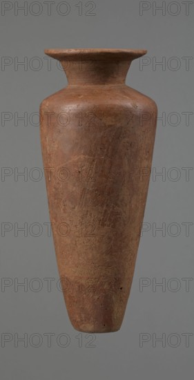 Vessel, Egyptian pottery, Type HS vessel, conical slender shape, widest at about 3/4 of the height. Shoulders wide, almost horizontal with slight slope. Neck wide, short, funnel-shaped in its lower part, widening toward the rim from about half its height. Rim wide, flat in the upper part, slightly rounded at the bottom, slightly asymmetrical. Bottom flat, slightly asymmetrical. Neck made separately and attached to the shoulders. Surface even; lower part finished to approximately 3/4 of its height with a knife or similar tool. Outer surface and inner surface of the rim and neck covered with dark red engobe and polished. Color dark red. Reconstructed from many original fragments; gaps filled with plaster. c. 2686–c. 2181 BC Old Kingdom, Edfu, vessel; height 24.8 cm, rim diameter 8.9 cm, shoulder diameter 10.3 cm, bottom diameter 4.1 cm., A tall, narrow clay vessel with a flared rim and a tapered base is shown against a plain gray background; the vessel has a rough, weathered surface with...