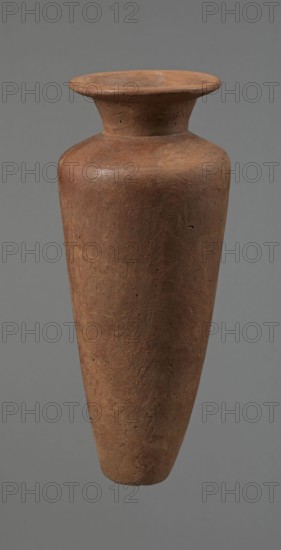 Vessel, Egyptian pottery, Type HS vessel of a conical, slender shape, widest at about 3/4 of the height. Shoulders quite wide, almost horizontal—slightly sloping. Neck wide, short, funnel-shaped in its lower part, widening toward the rim from about half its height. Rim wide, flat in the upper part, slightly rounded at the bottom, slightly asymmetrical. Bottom flat, slightly asymmetrical. Neck made separately and attached to the shoulders. Surface even. Lower part finished to approximately 3/4 of its height using a knife or similar tool. Outer surface and inner surface of the rim and neck covered with a layer of dark red engobe and polished. Color dark red. Vessel reconstructed from many original fragments; gaps filled with plaster. c. 2686–c. 2181 BC; Old Kingdom, Edfu. Vessel: height 24.8 cm; rim diameter 8.9 cm; shoulder diameter 10.3 cm; bottom diameter 4.1 cm., A single tall, tapered ceramic vessel with a wide, flared rim and narrow neck, shown against a plain gray background; the ...