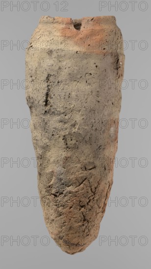 Vessel, Egyptian pottery, hand-made clay vessel with a conical belly widest in its upper part approximately 4/5 of the vessel's height. Rounded bottom. Irregularly marked shoulders—clearly sloping on one side and short, almost horizontal on the opposite. Straight, slightly tapering rim. Made of Nile clay with numerous organic inclusions and limestone particles visible on the surface. Uneven surface with numerous depressions; brown color. Quite well preserved; surface cracks resulting from poor clay kneading. Ca. 2686–2181 BC Old Kingdom, from Edfu. Vessel; height 38 cm, rim diameter 11.7 cm, body diameter 15.7 cm., An elongated, irregularly textured object with a rough, cracked surface in shades of beige, tan, light brown, and areas of reddish-orange, set against a plain gray background; the surface shows small pits, grooves, and rough patches with subtle darker speckles and variations, and the top edge is uneven with a small notch while the overall form tapers toward a rounded point a...