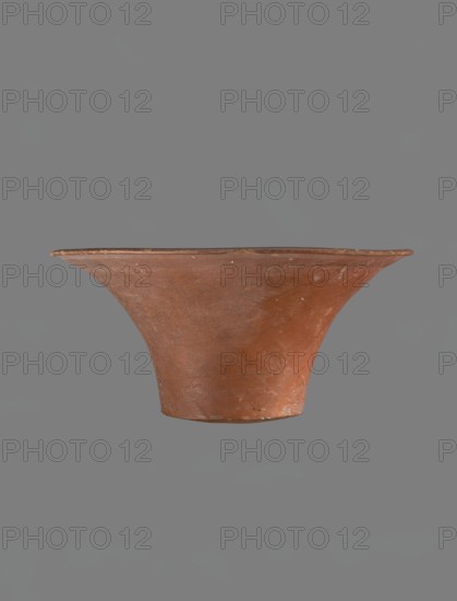 Bowl, Deep, cup-shaped clay bowl with a slightly convex bottom and sides arching upwards; straight, flat-topped flaring rim. Made of Nile clay NB1, per Vienna System, covered with an engobe mixed with red ochre and thoroughly polished; vessel color red. Well-preserved with slight damage to clay on the rim. Comparative references attribute similar forms to Old Kingdom contexts Late 4th–6th dynasties. Vessel dimensions: height 13.8 cm; rim diameter 28.8 cm; bottom diameter 11.9 cm., A wide, shallow bowl-like object made of reddish-brown clay with a flared rim and a narrower base, shown against a uniform gray background; the clay surface displays variations in tone with areas of lighter and darker reddish-brown and small spots of wear.