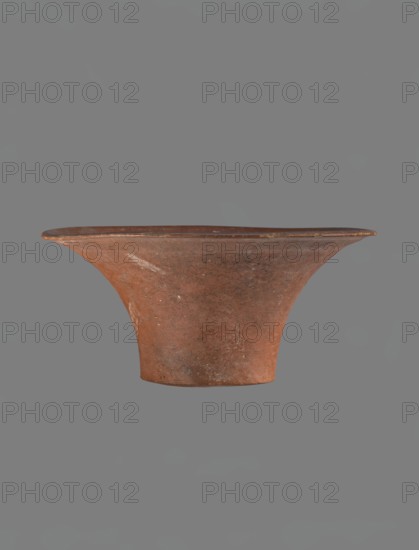 Bowl, Egyptian pottery, clay vessel — deep, cup-shaped bowl with a slightly convex bottom and sides arching upwards; straight rim, flat on top, flaring. Made of Nile clay NB1? and covered with an engobe containing red ochre and thoroughly polished. Vessel color: red. Well-preserved with slight damage to clay on the rim. Comparative material cites parallels from IV–VI dynasty and late VI dynasty contexts; typologically dated to the Old Kingdom ca. 2686–2181 BC. Place of origin: Edfu. Dimensions: height 13.8 cm; rim diameter 28.8 cm; bottom diameter 11.9 cm., A single wide-brimmed pottery bowl with a flared rim and a narrow base suspended against a neutral background; the vessel has an earthy reddish-brown color with patches of darker brown and small pale spots, a slightly rough textured surface showing subtle irregularities and wear, and the rim appears thinner and slightly darker than the body.