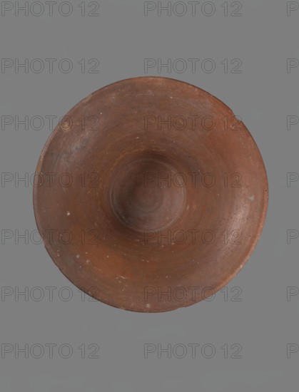 Bowl, Deep, cup-shaped bowl with a slightly convex bottom and sides arching upwards; straight, flat-topped, flaring rim. Made of Nile clay NB1 ?. Covered with an engobe containing red ochre and thoroughly polished. Red color. Well-preserved, with slight damage to the rim. Comparative references suggest parallels from the Old Kingdom IV–VI dynasties, ca. 2686–2181 BC. From Edfu. Dimensions: height 13.8 cm; rim diameter 28.8 cm; bottom diameter 11.9 cm., A round, shallow bowl with a concave center sits against a flat background; the bowl is primarily brown with areas of darker and lighter brown variations and small pale flecks, and the background is a uniform gray.