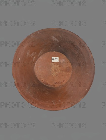 Bowl, Deep, cup-shaped clay bowl with a slightly convex bottom and sides arching upwards; straight, flat-topped flaring rim. Made of Nile clay NB1 ?. Covered with an engobe containing red ochre and thoroughly polished. Color: red. Well-preserved with slight damage to the rim. Ceramic vessel, Old Kingdom ca. 2686–2181 BC, height 13.8 cm; rim diameter 28.8 cm; bottom diameter 11.9 cm. Comparative references: parallels cited to Mycerinus, Giza Necropolis II, Qau and Badari pottery types IV–VI dyn., Abydos Middle Cemetery late VI dynasty, Umm el-Qaab no. 85 IV dynasty, and Asyut pottery chronologies. Origin: Edfu., A single round bowl viewed from above with a broad rim and a concave interior, showing a worn terracotta surface in shades of reddish-brown and clay brown with patches of darker brown and faint lighter scuffs; a small rectangular lighter patch is visible near the center of the bowl's interior; the background is a uniform gray.