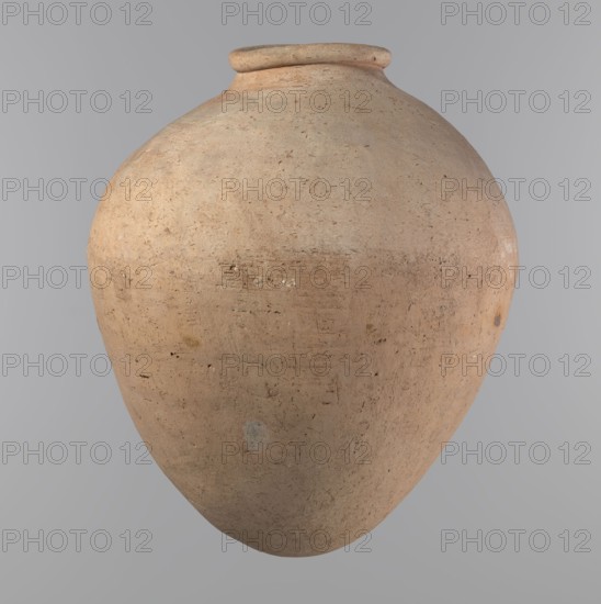 Vessel, unknown author. Egyptian pottery vessel of ovoid, slightly downward-stretched shape, widest at about 2/3 of the height. Broad, sloping shoulders, very short, wide neck. Roller-shaped rim, oval in cross-section, slightly flaring. Rounded bottom. Clay NB2 according to the Viennese System with significant organic admixture. Hand-made from two parts and joined at about 2/3 of the height; upper part turned. Surface leveled, possibly covered with a layer of engobe; traces of a white substance in places on the outer surface and on the rim. Beige color. Well-preserved. Ca. 2686–2181 BC; Old Kingdom, Edfu. Vessel. Height 34.6 cm; rim diameter 11.6 cm; body diameter 29 cm., A large rounded clay vessel with a narrow rim and bulbous body sits against a neutral background; the vessel shows a rough, textured surface with uneven patches and small pits and scratches. The colors visible are tan, beige, light brown, and hints of gray with slightly darker speckles and faint orangey-brown variatio...