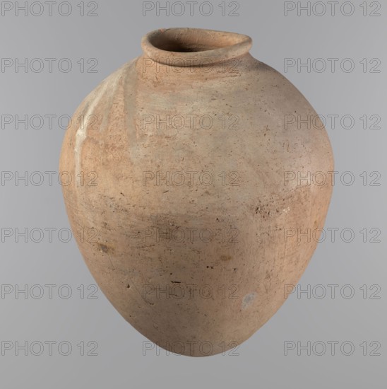 Vessel, Egyptian pottery, ceramic clay vessel of an ovoid, slightly downward-stretched shape, widest at about 2/3 of the height. Broad, sloping shoulders, very short wide neck. Roller-shaped rim, oval in cross-section, slightly flaring. Rounded bottom. NB2 clay Viennese System with a significant amount of organic admixture. Hand-made from two parts and joined at about 2/3 of the height; turned in the upper part. Surface leveled possibly covered with a layer of engobe. Traces of a white substance in places on the outer surface of the body and on the rim. Vessel color beige. Well-preserved. ca. 2686–ca. 2181 BC; Old Kingdom, Edfu; vessel; height 34.6 cm; diameter 11.6 cm rim, 29 cm body., A large rounded clay vessel with an open circular mouth and a turned rim, shown against a plain light gray background; the pot has a textured surface with an earthy palette of tan, light brown, beige, and subtle pale gray patches, with areas of darker brown speckles and occasional small darker spots, an...