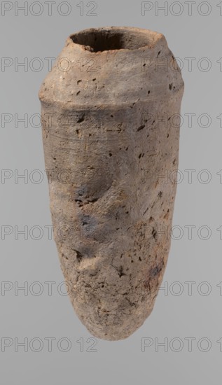 Vessel, Egyptian pottery, hand-made clay vessel, ceramics, vessel, Old Kingdom, c. 2686–c. 2181 BC; from Edfu. Vessel, height 33.5 cm, diameter 10.4 cm rim, diameter 15.1 cm body., A tall, cylindrical earthen vessel with a rough, pitted surface and an uneven rim, shown against a plain gray background; the vessel has a weathered texture with small holes and indentations and subtle irregularities in shape, and its colors include shades of brown, tan, beige, gray, and touches of reddish-brown.