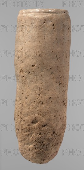 Vessel, Egyptian pottery, hand-made clay vessel, almost cylindrical, widest just below a straight, tapering rim; rounded bottom; slightly marked, irregular, very narrow sloping shoulders. Handmade from Nile clay with numerous organic inclusions and limestone particles visible on the surface; uneven surface, better worked in the upper part; carelessly made with numerous uneven depressions, especially on the bottom. Brown color. Fairly well preserved; surface cracks resulting from craftsmanship, kneading and firing. Old Kingdom, ca. 2686–2181 BC; from Edfu. Vessel, height 36.5 cm; diameter 11.5 cm rim, 13.2 cm body., A roughly cylindrical, elongated object with a textured, pitted surface fills the frame against a plain gray background; the object appears earthy and irregular with a rough, porous texture and small holes, indentations, and surface cracks, showing a dominant tan or light brown color with subtle variations of darker brown and tiny flecks of gray, and a slightly rounded top e...