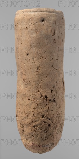 Vessel, Egyptian pottery, ceramics, clay vessel, hand-made. An almost cylindrical vessel, widest in its upper part just below the rim. The bottom is rounded. The shoulders are slightly marked, irregular, very narrow, and sloping. The rim is straight, tapering. Handmade of Nile clay with numerous organic inclusions and limestone particles visible on the surface. The surface is uneven and better worked in the upper part. Carelessly made, with numerous uneven depressions on the surface, especially at the bottom. Color: brown. Fairly well preserved; surface cracks attributable to careless kneading of the clay and firing. ca. 2686–ca. 2181 BC; Old Kingdom, Edfu. Vessel; height 36.5 cm; diameter 11.5 cm rim, 13.2 cm body., A tall, cylindrical object with a rough, porous surface in shades of light brown and tan, showing irregular pits, small indentations, and scattered darker brown spots; the surface texture varies from smoother areas near the top to more cracked and crumbly regions toward th...