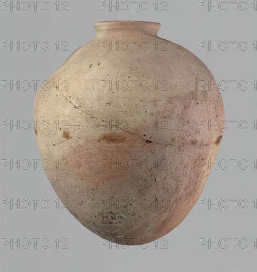 Vessel, Egyptian pottery, ceramic clay vessel of an ovoid, slightly downward-stretching shape, widest at about 2/3 of the height. Broad, sloping shoulders, very short, wide neck. Rounded rim, slightly profiled in the lower part, oval in cross-section, slightly flaring. Rounded bottom. Just above the widest diameter there is a dent made before the vessel was fired. Clay NB2 Vienna System with a significant amount of organic admixture. Wheel-made; approximately half of its height was worked with a knife or similar tool. Beige. Cracked in the upper part. Old Kingdom, c. 2686–c. 2181 BC; Edfu. Vessel. Height 34 cm; rim diameter 10.5 cm; body diameter 29 cm., A large rounded ceramic vessel with a narrow neck and flared lip, shown against a plain gray background; the surface of the vessel displays a weathered, matte texture with visible scratches and small pits, and areas of color including light beige, pale pink, dusty rose, muted orange, and small patches of darker brown; there are faint l...