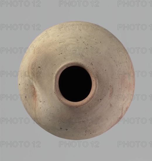 Vessel, Egyptian pottery, ceramics, clay vessel. Ovoid, slightly downward-stretching shape, widest at about 2/3 of the height. Broad, sloping shoulders, very short, wide neck. Rounded rim, slightly profiled in the lower part, oval in cross-section, slightly flaring. Rounded bottom. Just above the widest diameter of the vessel there is a dent made before the vessel was fired. Clay NB2 according to the Vienna System with a significant amount of organic admixture. Wheel-made, with approximately half of its height worked with a knife or similar tool. Beige. Cracked in the upper part. c. 2686–c. 2181 BC; Old Kingdom, Edfu. Vessel. Height 34 cm; rim diameter 10.5 cm; body diameter 29 cm., A round ceramic vessel viewed from above with a circular opening in the center and smooth curved sides showing a textured surface; the vessel displays a range of beige, tan, light brown, and subtle reddish tones with small darker speckles and patches, set against a uniform light gray background.
