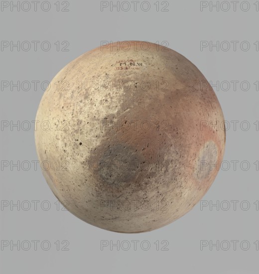 Vessel of an ovoid, slightly downward-stretching shape, widest at about 2/3 of the height. Broad, sloping shoulders, very short, wide neck. Rounded rim, slightly profiled in the lower part, oval in cross-section, slightly flaring. Rounded bottom. Just above the widest diameter of the vessel there is a dent made before the vessel was fired. Clay NB2 according to the Vienna System with a significant amount of organic admixture. The vessel was wheel-made, with approximately half of its height worked with a knife or similar tool. The vessel is beige and is cracked in the upper part. c. 2686–c. 2181 BC; Old Kingdom, Edfu; vessel. Height 34 cm; rim diameter 10.5 cm; body diameter 29 cm., A roughly spherical object fills most of the image, showing a weathered, pitted surface with a mix of beige, tan, light brown, reddish-brown, gray, and faint pink tones; the surface has several darker circular patches and areas of mottled discoloration, with small pits and speckles scattered across it, and t...