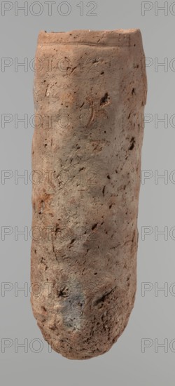 Vessel, An almost cylindrical handmade Nile-clay vessel, widest just below a straight, slightly tapering rim; rounded bottom; shoulders almost illegible. Made of not-well-worked Nile clay with numerous organic inclusions and limestone particles visible on the surface. Carelessly made with uneven depressions, especially at the bottom; brown in color; cracks on the surface due to workmanship and firing. Ceramic vessel, clay; Old Kingdom, ca. 2686–ca. 2181 BC; Edfu. Height 37.9 cm; diameter 11.4 cm rim, 12.5 cm body., An elongated cylindrical clay object with an uneven, rough surface showing a mix of reddish-brown, tan, gray, and faint darker brown tones, pitted and marked with small holes, cracks, and irregular indentations across its surface, with a slightly flattened top rim and a rounded bottom, photographed against a plain light gray background.