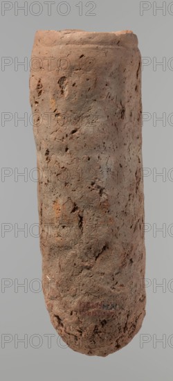 Vessel, Egyptian pottery, handmade clay vessel. An almost cylindrical vessel, widest in its upper part just below the straight, slightly tapering rim; rounded bottom; shoulders almost completely illegible. Made of Nile clay with numerous organic inclusions and limestone particles visible on the surface. Carelessly made, with numerous uneven depressions on the surface, especially at the bottom; brown in color; cracks on the surface resulting from workmanship and firing. Old Kingdom, ca. 2686–2181 BC; from Edfu. Vessel; height 37.9 cm, diameter 11.4 cm rim, diameter 12.5 cm body., A vertical, cylindrical object with an uneven, rough surface that appears to be made of a porous, earthen material; the surface shows a variety of pits, grooves, and small cavities and has an irregular, slightly tapered form with a rounded bottom and a flatter top edge. The visible colors are shades of brown ranging from light tan to deeper reddish-brown, with small areas of darker brown and hints of muted gray...