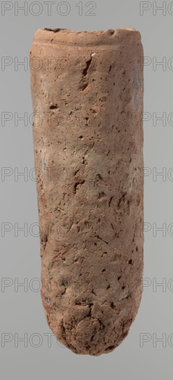 Vessel, Egyptian pottery vessel, handmade clay vessel. An almost cylindrical vessel, widest in its upper part just below the rim; rounded bottom; shoulders largely illegible; straight, slightly tapering rim. Handmade of Nile clay with numerous organic inclusions and limestone particles visible on the surface; carelessly made with uneven depressions, especially at the bottom; brown color; preserved though surface cracks result from careless kneading and firing. Old Kingdom, ca. 2686–2181 BC; from Edfu. Height 37.9 cm; diameter 11.4 cm rim, 12.5 cm body., A vertical cylindrical object with an uneven, rough surface that appears handmade, shown against a plain neutral background; the surface shows many small pits, indentations, and irregularities with areas of slight bulging and depressions, and the top edge is uneven and slightly rounded while the bottom tapers and is more textured and rough; visible colors include shades of brown, light brown, reddish-brown, and small patches of pale gra...