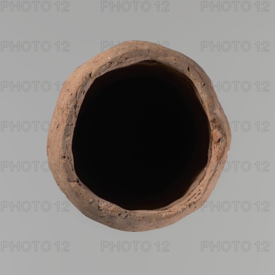 Vessel, Egyptian pottery vessel, clay, hand-made; almost cylindrical, widest just below a straight, slightly tapering rim; rounded bottom; shoulders almost illegible. Handmade of Nile clay with numerous organic inclusions and limestone particles visible on the surface; carelessly made with uneven depressions, especially at the bottom; brown color; cracks on the surface resulting from workmanship and firing. Old Kingdom, ca. 2686–ca. 2181 BC; from Edfu. Height 37.9 cm; diameter 11.4 cm rim, 12.5 cm body., A top-down view of a round, hollow clay vessel with a rough, uneven rim in shades of brown and terracotta surrounding a deep black interior, set against a smooth light gray background.