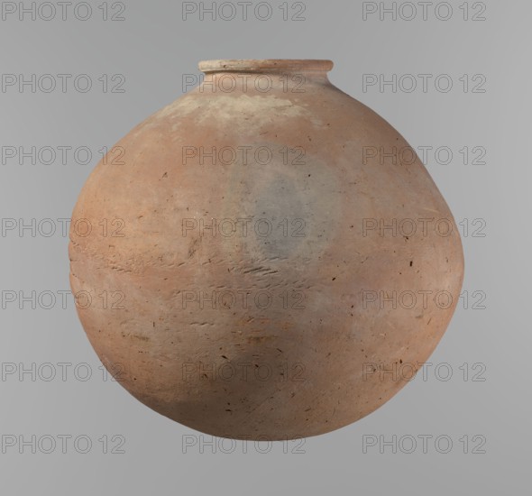 Vessel, Egyptian pottery, ceramics, clay vessel. A vessel with an almost spherical, slightly horizontally stretched shape, widest about half the height. Broad, sloping shoulders, very short neck. Rounded rim, oval in cross-section, slightly flaring. Rounded bottom. Horizontal cord impressions at the widest point of the vessel. NB2 clay according to the Vienna System with a significant amount of organic admixture. The surface of the vessel is smooth. Made on a wheel; approximately half of its height was worked with a knife or similar tool. Colour beige. Very well preserved. Old Kingdom, ca. 2686–ca. 2181 BC; Edfu. Vessel, height 28.5 cm, rim diameter 10.4 cm, body diameter 30.4 cm., A large round clay pot with a short narrow neck and slightly flared rim fills the frame, showing a textured surface with a weathered, matte finish; the pot displays a range of earthy colors including terracotta, light brown, beige, pale gray, and hints of muted orange, with subtle patches and streaks of dark...