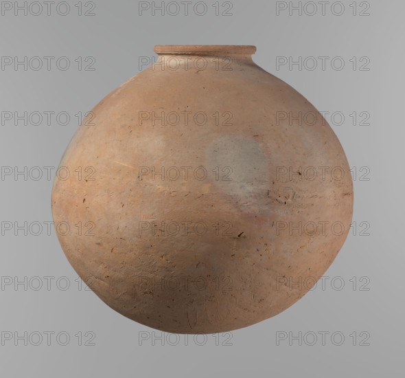 Vessel, Egyptian pottery vessel, clay, ca. 2686–ca. 2181 BC Old Kingdom, from Edfu. Almost spherical, slightly horizontally stretched shape, widest about half the height; broad, sloping shoulders, very short neck. Rounded rim, oval in cross-section, slightly flaring; rounded bottom. Horizontal cord impressions at the widest point. Made on a wheel; approximately half the height was worked with a knife or similar tool. NB2 clay Vienna System with significant organic admixture. Smooth surface. Beige color. Very well preserved. Height 28.5 cm; rim diameter 10.4 cm; body diameter 30.4 cm., A large rounded clay vessel occupies the center of the image, showing a matte, slightly rough surface in shades of terracotta, light brown, and muted peach with subtle patches of pale gray and faint pink. The vessel has a narrow, short neck with a small rim that is a slightly darker brown, and the body displays small dark flecks and irregular speckles across its surface as well as faint scratches and text...