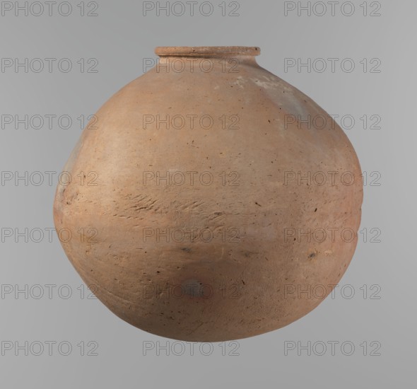 Vessel, Egyptian pottery vessel, clay, wheel-made with roughly half of its height worked with a knife or similar tool. Almost spherical, slightly horizontally stretched shape, widest about half the height; broad sloping shoulders, very short neck; rounded rim oval in cross-section and slightly flaring; rounded bottom. Horizontal cord impressions at the widest point. NB2 clay Vienna System with significant organic admixture; smooth surface. Beige color. Very well preserved. Old Kingdom, ca. 2686–2181 BC; Edfu. Height 28.5 cm; rim diameter 10.4 cm; body diameter 30.4 cm., A large rounded clay vessel with a narrow rim and bulbous body suspended against a light gray background; the vessel shows a textured, slightly rough surface with visible tool marks and small pits, and colors include terracotta, light brown, pale orange, muted grayish patches, and hints of darker brown speckles.