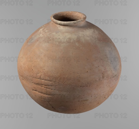 Vessel, Egyptian pottery, ceramic clay vessel. A nearly spherical vessel slightly stretched horizontally, widest about half the height; broad sloping shoulders, very short neck, rounded rim oval in cross-section slightly flaring, and rounded bottom. Horizontal cord impressions at the widest point. NB2 clay Vienna System with significant organic admixture; surface smooth. Made on a wheel; approximately half the height was worked with a knife or similar tool. Beige color. Very well preserved. Old Kingdom, ca. 2686–ca. 2181 BC; Edfu. Vessel; height 28.5 cm, rim diameter 10.4 cm, body diameter 30.410 cm., A round clay vessel with a narrow open neck and flared rim, showing an uneven, textured surface with visible scratches and chips; the vessel displays a mix of earthy terracotta, beige, pale gray, and subtle brown tones, with areas of lighter discoloration and darker smudges, set against a smooth gray background.
