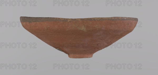 Bowl, Egyptian painted pottery bowl with conical shape and ring-shaped foot. Straight rim slightly flaring outward, irregular. Wheel-made of Nile clay type ND Vienna System. Surface even, covered with glaze before firing; inner and outer rim bear a narrow ~0.5 cm black band; remainder red. Traces of polish; glaze slightly worn in places possible use-wear. Good condition with minor clay chips on rim and abrasions over surface. Analogies: Egypt's Golden Age no. 51, p. 78, ca. 1550–ca. 1425 BC; New Kingdom, early 18th Dynasty. Possible find places: Edfu, Deir el-Medina. Vessel: height 5.3 cm; diameter 15.1 cm rim; diameter 3.1 cm bottom., A shallow, wide bowl viewed from the side with a tapered base and a slightly flared rim, showing a rough, weathered surface in terracotta and reddish-brown tones with areas of darker brown along the rim and small patches of lighter beige where the surface is worn; the background is a uniform pale gray.