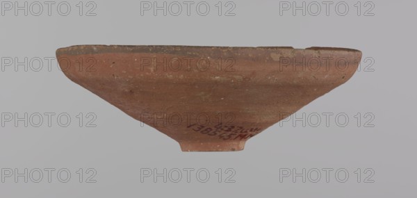 Bowl, Egyptian painted pottery bowl with a conical shape and a ring-shaped foot. Straight rim, slightly flaring outward, irregular. Wheel-made from Nile clay type ND, Vienna System. Surface even, covered with glaze before firing. Narrow approx. 0.5 cm black band of decoration on the inner and outer rim; remainder of vessel red. Traces of polish on the surface; glaze slightly worn in places possible use-wear. Good condition with minor clay chips on the rim and abrasions over the surface. Analogies: Egypt's Golden Age no. 51, p. 78, ca. 1550–1425 BC; New Kingdom, early 18th Dynasty. Possible findplaces: Edfu, Deir el-Medina . Vessel; height 5.3 cm; rim diameter 15.1 cm; base diameter 3.1 cm., A shallow bowl-like object viewed from the side with a flared rim and a narrow foot, showing an overall reddish-brown clay surface with patches of darker brown and lighter beige speckles and wear; the rim edge appears darker and slightly rough, and there is visible surface texture and small pits acr...