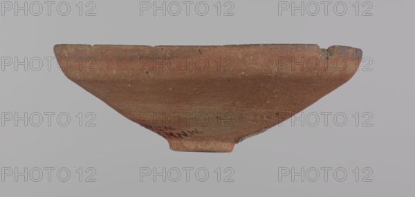 Bowl, Painted pottery, clay bowl with conical shape and ring-shaped foot. Straight rim slightly flaring outward, irregular. Wheel-made from Nile clay type ND, Vienna System. Surface even, covered with glaze before firing; inner and outer rim bear a narrow ~0.5 cm black decorative band; remainder of vessel is red. Traces of polish; glaze slightly worn in places possible use-wear. Good condition with minor clay chips on rim and abrasions overall. Analogies: Egypt's Golden Age no. 51, p. 78, ca. 1550–1425 BC; New Kingdom, early 18th Dynasty. Provenance possibly Edfu or Deir el-Medina. Vessel: height 5.3 cm; rim diameter 15.1 cm; base diameter 3.1 cm., A shallow, wide bowl-shaped ceramic fragment with a rounded rim and a small raised foot, shown against a pale gray background; the ceramic surface is mainly terracotta with variations of reddish-brown and patches of lighter tan and beige, and there are areas of darker brown along the rim and a chipped section at one edge revealing a rougher ...