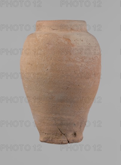 Vessel, Beer jug of a slightly irregular, conical shape with a wide, very short neck and a flat bottom. Flat, narrow shoulders and a gently rounded, straight rim. Wheel-made of Nile clay type NB2 Vienna System. Bottom cut off with string and bearing clear potter's fingerprints, flaring slightly in its lowest part. Surface even. Color: red. Complete and fairly well preserved, with minor damage to the bottom. New Kingdom, ca. 1550–1069 BC, provenance: Edfu. Dimensions: height 24 cm; rim diameter 10 cm; body diameter 16 cm; bottom diameter 9.2 cm., A large rounded ceramic vessel with a narrow flat rim and a tapered base sits against a plain background; its surface shows a rough, grainy texture with areas of unevenness and small pits, and there are visible cracks and chips near the base and along the body. The vessel displays earthy tones of brown, tan, beige, and hints of reddish-orange, with subtle variations and mottling across the surface.