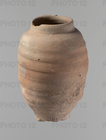 Vessel. Beer jug of a slightly irregular, conical shape with a wide, very short neck and a flat bottom. Flat, straight rim. Wheel-made from Nile clay of type NB2-ND Vienna System. Bottom is cut off with string, with clear potter's fingerprints around the bottom. Surface even. Clay color red. Vessel complete, fairly well preserved, with minor damage to the rim and small chips on the surface. Ca. 1550–1069 BC New Kingdom, Edfu. Vessel. Height 24.4 cm; rim diameter 9.8 cm; body diameter 16.3 cm; bottom diameter 8.5 cm., A large rounded clay vessel with an open top and a rough, uneven rim sits against a plain light gray background; the vessel shows a textured surface with wheel-made horizontal ridges and patches of worn, pitted areas, with a color palette of light brown, tan, reddish-brown, and small traces of pale gray and white.