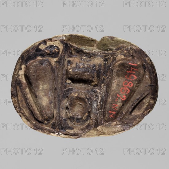 Scarab with the name Menkheperre. Scarab amulet with a decorated top engraved with a cartouche topped with two feathers containing the name Menkheperre i.e. Amun-Re. On the bottom of the scarab is another cartouche with the same name and two snakes turned inward. c. 1550–c. 1069 BC, New Kingdom, Western Thebes Valley of the Queens. Materials/function: scarab amulet; height 3.8 cm, width 2.7 cm., An oval carved object sits against a plain light gray background, showing a worn surface with rough textures and carved recessed shapes; the object displays a palette of browns, tans, dark brown to almost black areas, and a few small patches of red and off-white, with irregular contours and shallow grooves giving it an aged, uneven appearance.