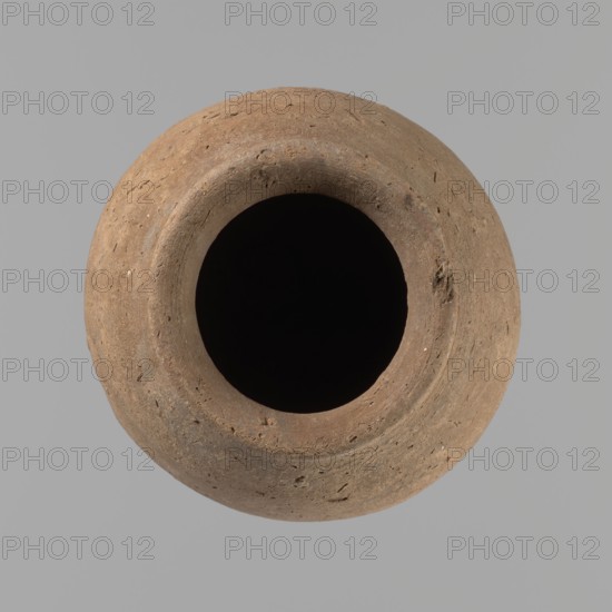 Vessel with hieratic inscription. Egyptian pottery, clay conical vessel tapering toward the bottom, slightly irregular; widest approx. 3/4 of the height. Narrow, sloping shoulders; short, wide neck; very gently rounded, widening rim; pointed bottom. Handcrafted; upper part shoulders, neck and rim turned. Around half the height a trace of the joining of two separately made parts. Surface leveled, outer probably covered with a layer of engobe. Made of Nile clay Vienna System. In the lower part of the belly there are remains of a hieratic inscription in black. Rim damaged. Analogies: Petrie, Dendera; Hope, Akhmim; Reisner, Mycerinus; Brunton, Qau and Badari; Mace, Naga ed-Der II; Reisner, Naga ed-Der III; Petrie, Abydos II; Keiser et al., MDAIK 40. Old Kingdom, ca. 2686–2181 BC. Findspot: Edfu. Dimensions: height 13.2 cm; rim diameter 5.8 cm; body diameter 8.3 cm., A round earthen vessel viewed from above with a wide dark opening at its center, showing a textured surface in shades of brow...